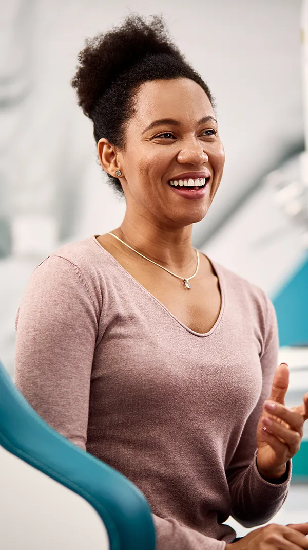 A patient smiles while consulting with a dentist in a modern dental clinic, with dental imagery visible on a screen in the background, illustrating positive patient outcomes.