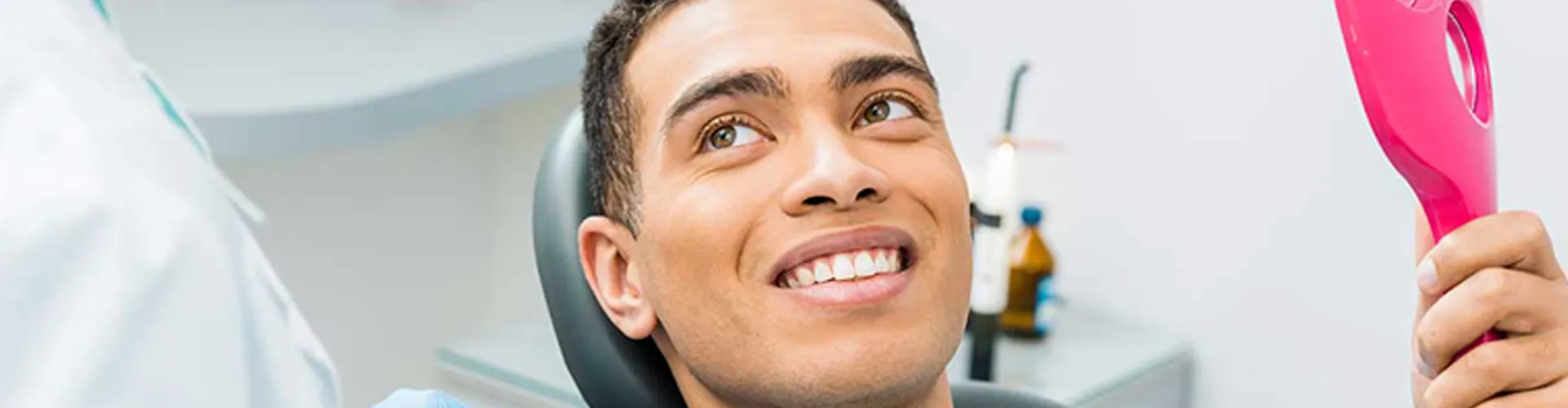 A man smiling while holding a mirror and looking at the dentist.