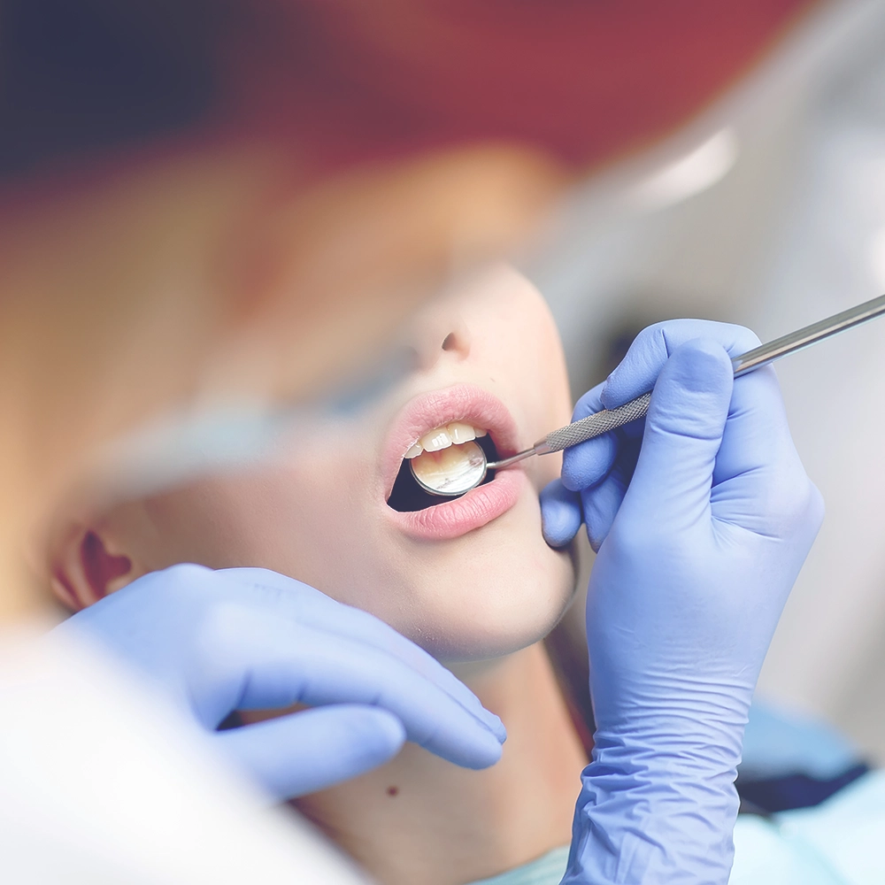 A dentist examines a patient's teeth with a dental mirror, highlighting patient care during a dental checkup.