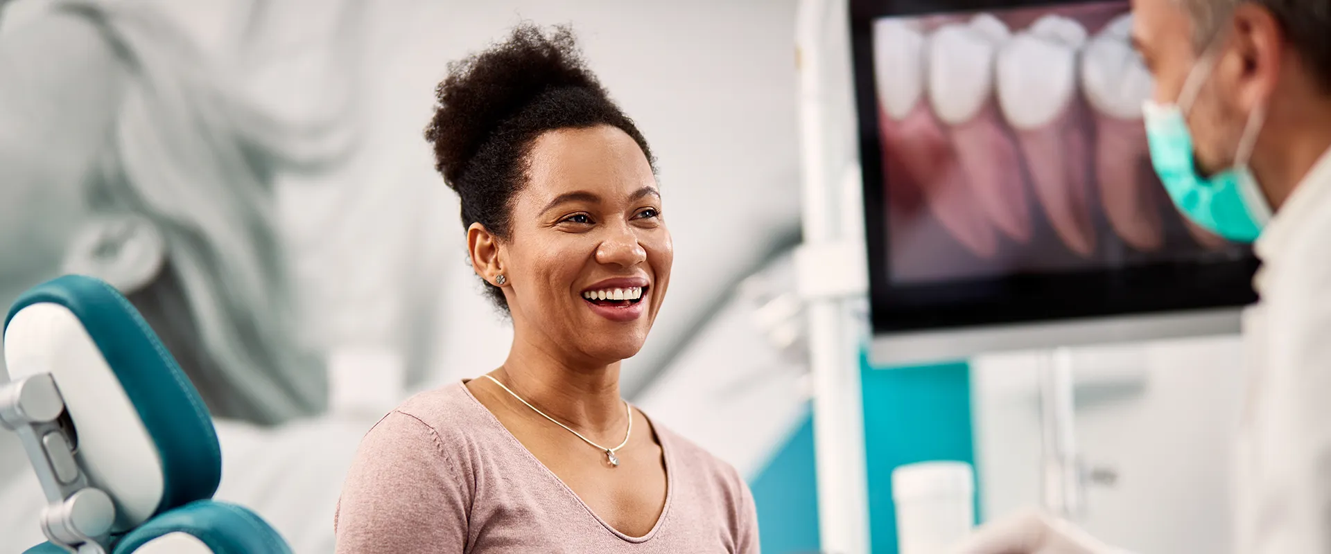 A patient smiles while consulting with a dentist in a modern dental clinic, with dental imagery visible on a screen in the background, illustrating positive patient outcomes.